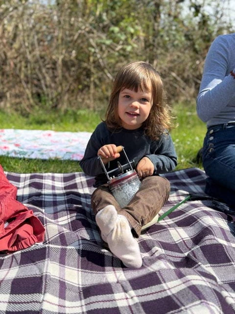 Ein Kind sitzt auf einer Decku und schlägt Butter