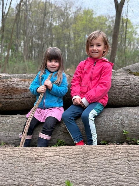 Zwei Kinder sitzen auf gefällten Baumstämmen